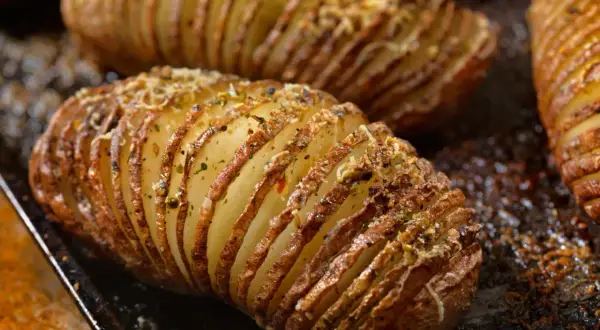 Pommes de terre nouvelles coupées en accordéon, dorées et garnies d'herbes et de fromage, prêtes à être dégustées.