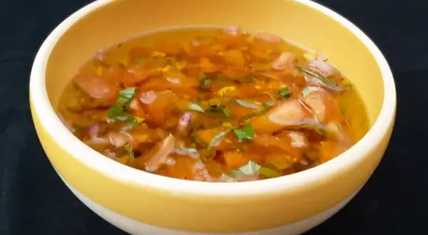 Un bol jaune contient une sauce vierge fraîche, avec des dés de tomates, des herbes vertes et une vinaigrette translucide.