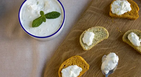 Un bol de tzatziki frais garni de menthe, servi avec des toasts. Une recette facile à partager !
