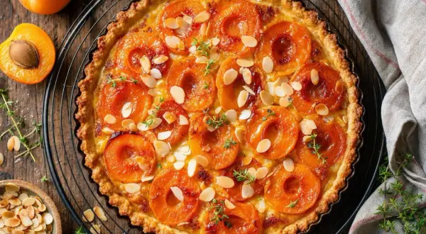 Une délicieuse tarte aux abricots classique, garnie d'amandes effilées et de thym frais, prête à être dégustée.