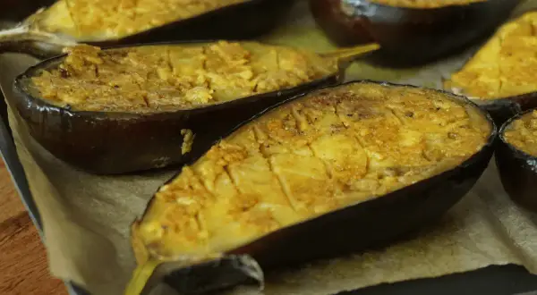 Aubergines au four, coupées en deux et garnies d'une préparation dorée, prêtes à être dégustées.