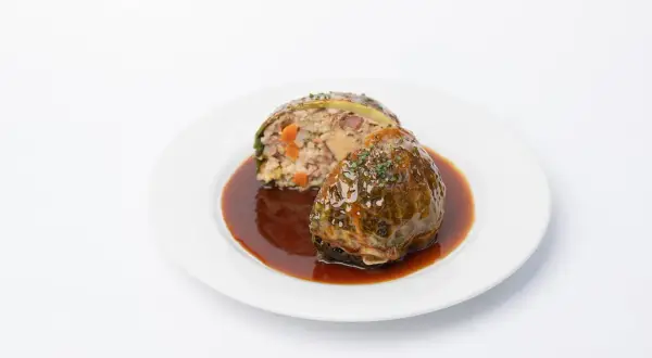 Chou farci, une recette du carnet de Julie, servi avec une sauce brune et garni d'herbes.