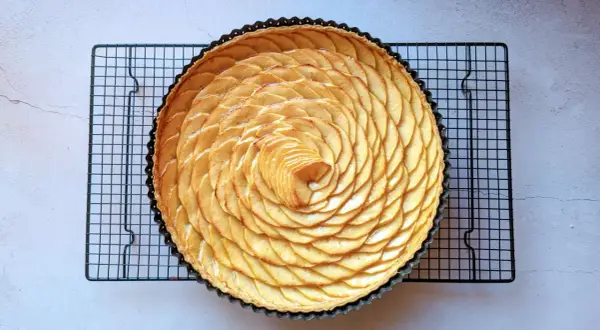 Tarte aux pommes recette de maman, magnifiquement décorée de fines tranches de pommes disposées en spirale sur une pâte dorée.