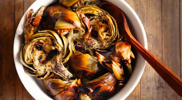 Artichauts barigoule à la façon Etchebest, rôtis et caramélisés, servis dans un plat blanc avec une cuillère en bois.