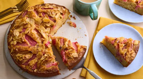Un délicieux dessert rhubarbe gastronomique, un gâteau aux amandes effilées et à la rhubarbe rose, servi sur une assiette bleue.