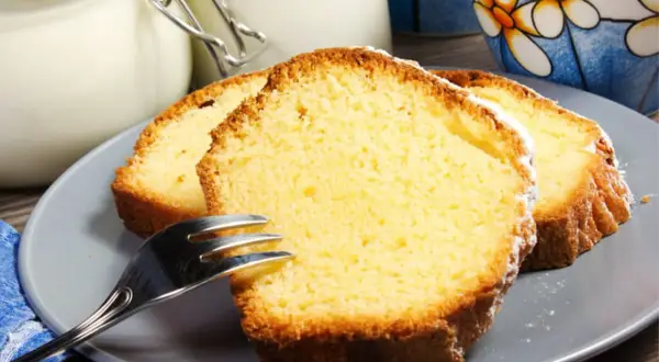 Tranches de gâteau au yaourt moelleux, saupoudrées de sucre glace, sur une assiette grise avec une fourchette.