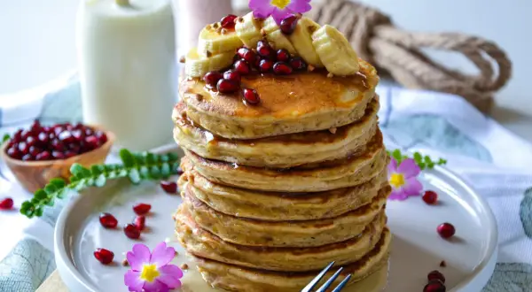 Pile de pancake banane, garnie de fruits rouges, de rondelles de banane et de fleurs roses. Un délice pour le petit-déjeuner.
