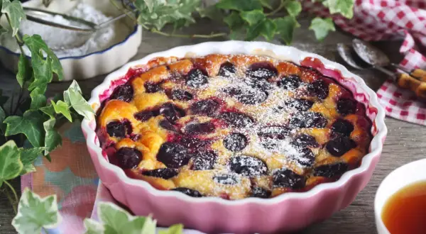 Un délicieux clafoutis aux prunes, saupoudré de sucre glace, prêt à être dégusté avec une tasse de thé.