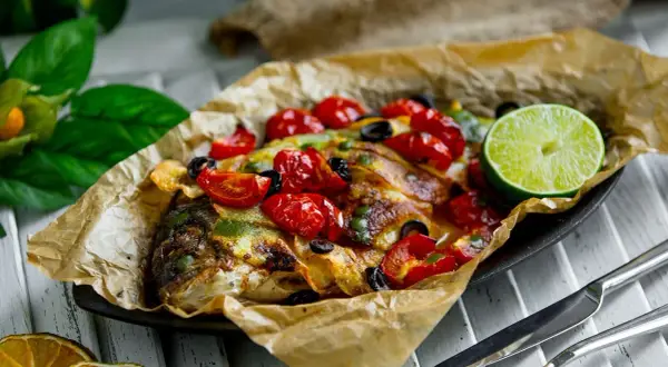 Dorade en papillote, savoureuse et colorée, garnie de tomates cerises, d'olives et d'une tranche de citron vert.