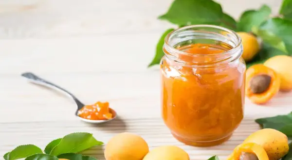 Un pot de confiture abricot peu sucrée, avec des abricots frais et une cuillère remplie de cette délicieuse confiture.
