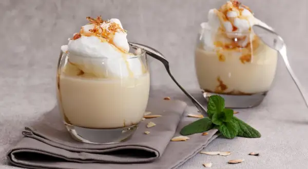 Deux verres de délicieux oeufs à la neige, surmontés de crème et de caramel, avec une touche de menthe fraîche.