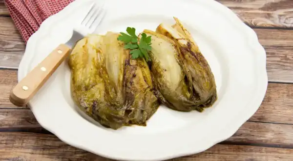 Deux endives fondue à la poêle, garnies de persil, sur une assiette blanche avec une fourchette.
