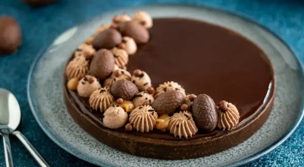Délicieuse tarte chocolat caramel, ornée d'œufs en chocolat et de touches de crème, prête à être dégustée.