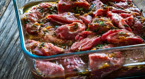 Morceaux de joue de porc marinés dans un plat en verre, prêts pour une délicieuse recette.