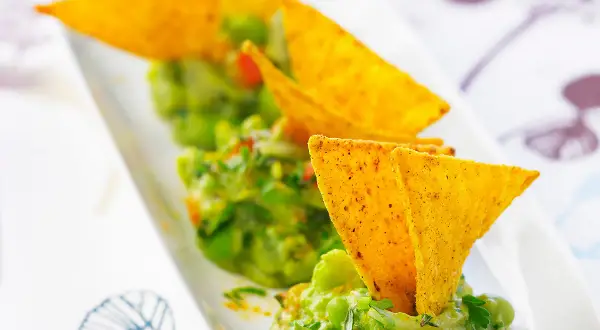 Guacamole maison, une recette facile et savoureuse. Des chips tortilla plongent dans ce délice vert.