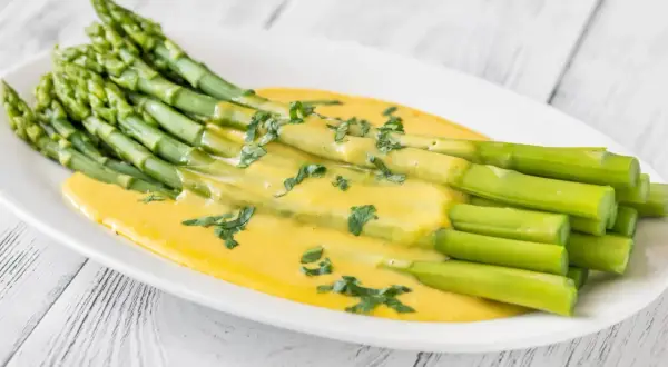 Asperges vertes fraîches nappées d'une sauce onctueuse et dorée, parsemées d'herbes. Un délice de sauce pour asperges chaudes.