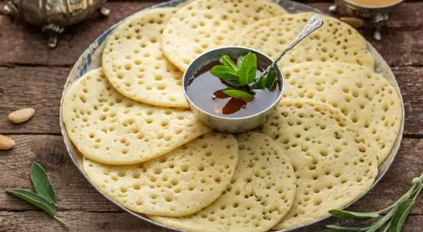 Une assiette de crêpes mille trous, garnie d'une coupelle de miel et de menthe fraîche, prête à être dégustée.