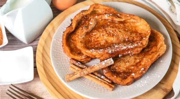 Trois tranches de pain perdu dorées, saupoudrées de sucre glace et garnies de bâtons de cannelle. Un délice pour le petit-déjeuner.