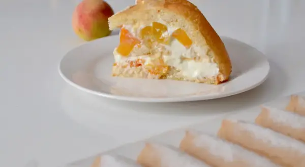 Tranche de charlotte aux fruits et fromage blanc, garnie de morceaux de pêche et de crème onctueuse. Un délice fruité et léger.