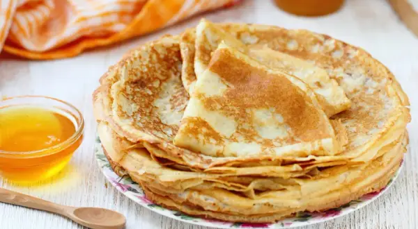 Pile de crêpes dorées, accompagnées d'un bol de miel. Parfait pour une recette pâte à crêpe facile sans repos.