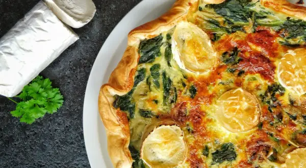 Tarte épinard chèvre dorée, avec du fromage de chèvre frais à côté et une touche de persil.