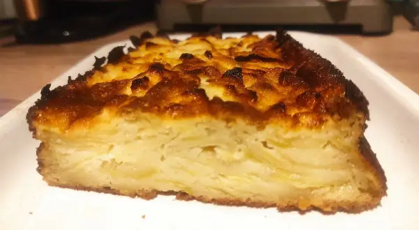 Tranche épaisse d'un délicieux cake aux pommes, avec une croûte dorée et caramélisée.
