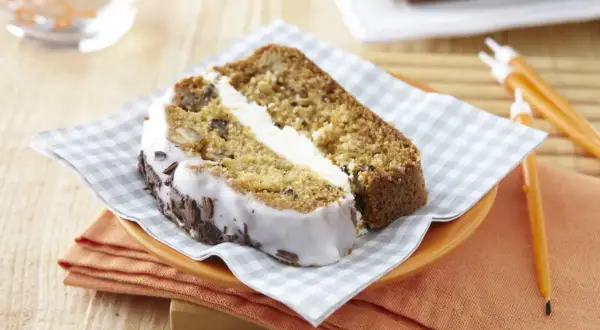 Tranche de carrot cake moelleux avec glaçage blanc et copeaux de chocolat. Un délice à savourer !