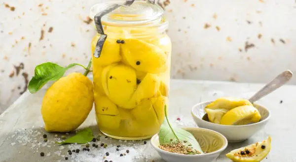 Un bocal de citrons confits au sel, prêts pour une recette citron confit sucre. Des épices et du gros sel parsèment la table.