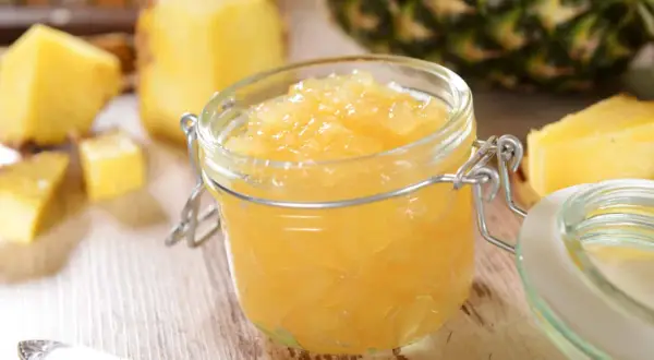 Un pot de confiture d'ananas maison, entouré de morceaux d'ananas frais et d'une cuillère.