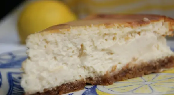 Tranche de cheesecake ricotta citron, crémeuse et légère, sur une assiette décorée de citrons.