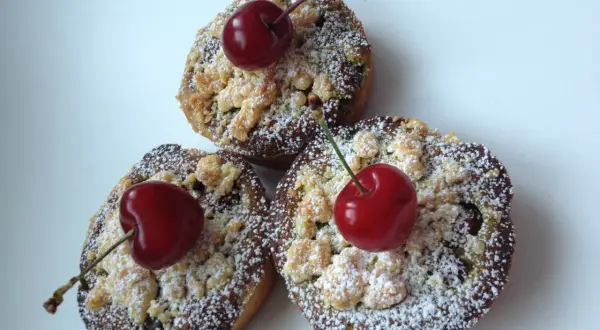 Trois petites tartelettes aux cerises, saupoudrées de sucre glace et ornées d'une cerise fraîche sur le dessus.