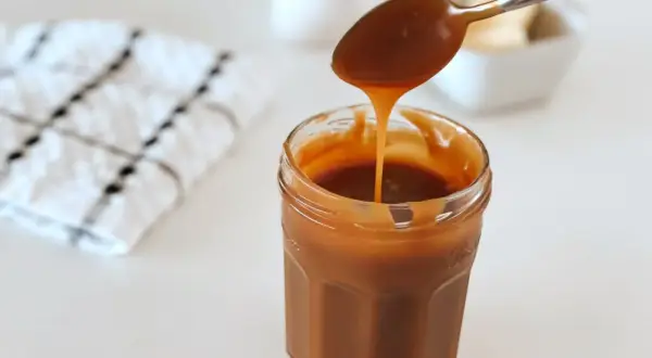 Une cuillère verse un caramel beurre salé onctueux dans un pot en verre.