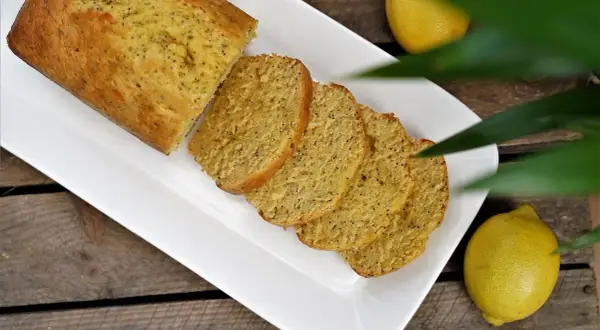 Un délicieux cake citron pavot, coupé en tranches, servi sur une assiette blanche, avec des citrons frais à côté.