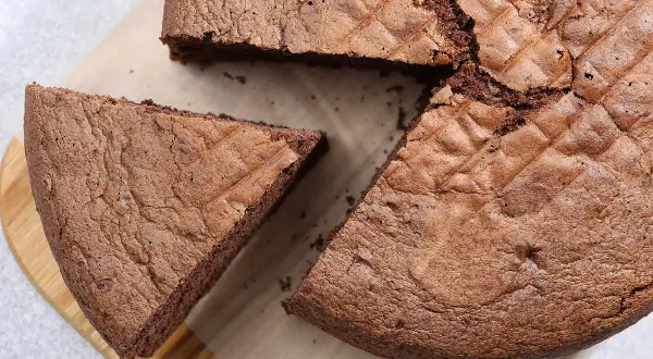 Un gâteau chocolat Pierre Hermé, moelleux et aérien, avec une part coupée sur une planche en bois.