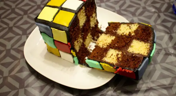 Un gâteau Rubik's cube, coupé en deux, révèle un intérieur marbré chocolat et vanille. Les couleurs vives du glaçage rappellent le célèbre casse-tête.