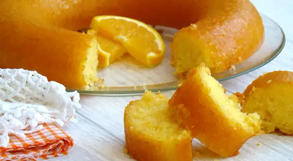 Un délicieux cake à l'orange, avec des tranches d'orange fraîche, servi sur une assiette en verre. Une part est déjà coupée.