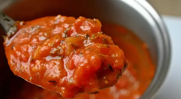 Une cuillère débordante de tomate concassée, parfumée d'herbes, prête à garnir un plat.