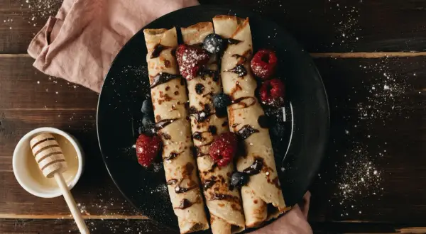 Crêpes roulées garnies de fruits rouges et de chocolat, prêtes à être dégustées. Une recette simple et gourmande pour le petit-déjeuner ou le goûter.