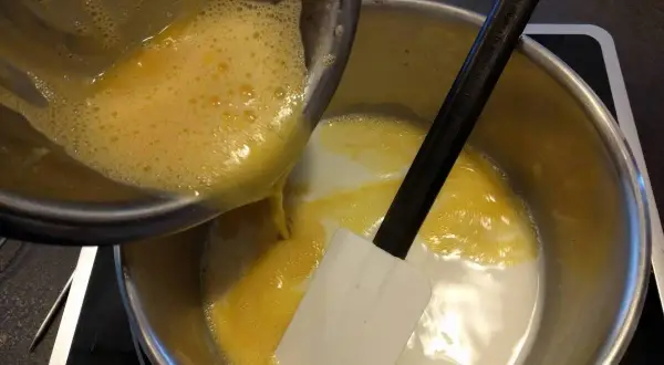 Préparation d'une recette crémeux vanille Michalak : on verse un mélange d'œufs battus dans une casserole contenant du lait et une spatule.