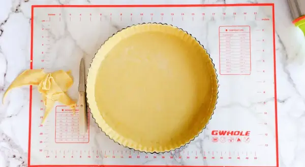 Pâte brisée salée prête à être garnie dans un moule à tarte. Des chutes de pâte et un couteau sont à côté.