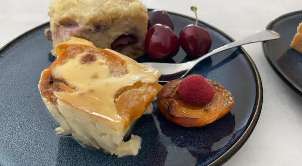 Un délice de clafoutis abricot, servi avec des cerises et une framboise sur une pêche rôtie.