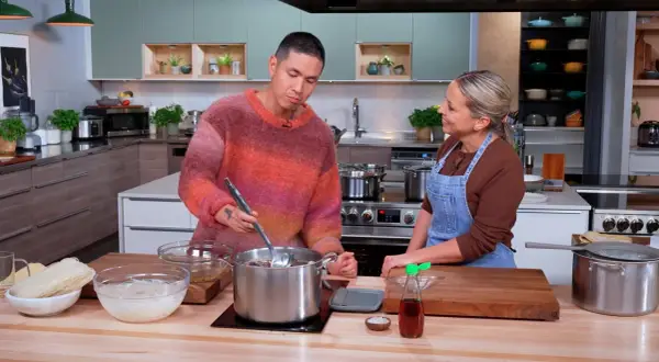 Un homme et une femme préparent un plat dans une cuisine. Le bouillon de poulet mijote dans une grande casserole.