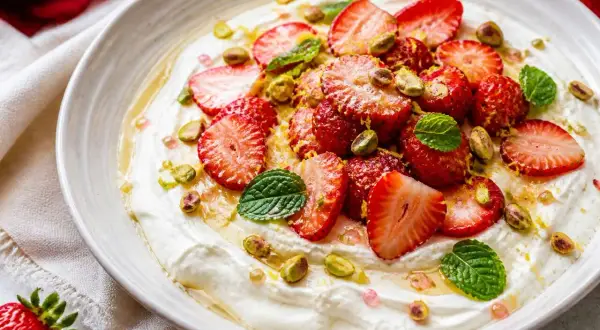 Délicieuse salade de fruits maison : fraises fraîches, pistaches croquantes et menthe fraîche sur une crème onctueuse, arrosée de miel.