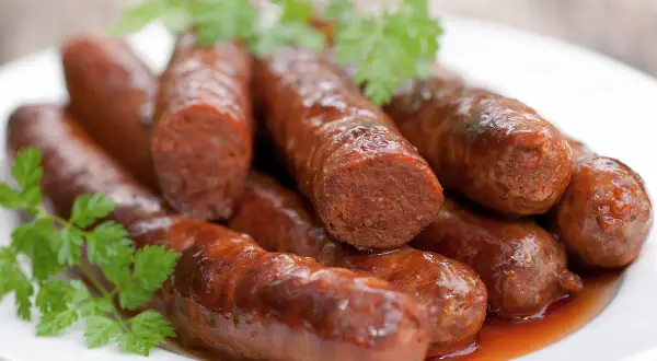 Assiette de merguez au four, dorées et juteuses, garnie de persil frais. Un délice prêt à être dégusté.