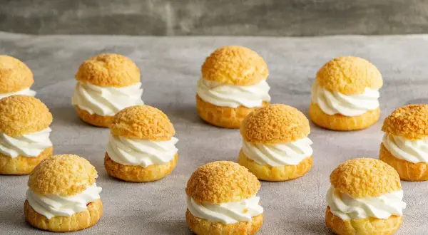 Douze petits choux garnis de crème fouettée, prêts à être dégustés. Ces délices de pâte à choux sont parfaits pour un goûter.