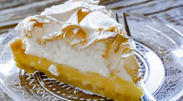 Une part de tarte au citron meringuée, avec sa crème jaune acidulée et sa meringue dorée, prête à être dégustée.