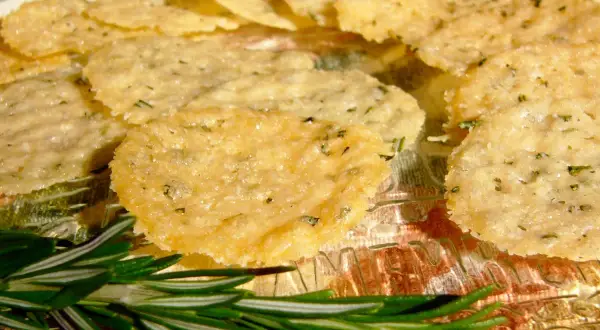 Délicieuses tuiles parmesan poêle, croustillantes et dorées, parsemées d'herbes. Une branche de romarin frais ajoute une touche aromatique.