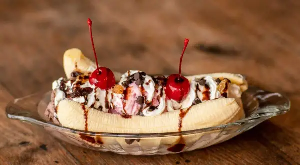 Un déliceux banana split garni de crème fouettée, de cerises et de sauce au chocolat, prêt à être dégusté.