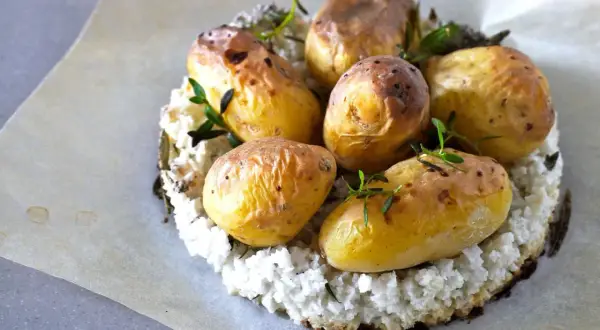 Pommes de terre nouvelles dorées, garnies d'herbes fraîches, sur un lit de purée de chou-fleur. La cuisson pomme de terre nouvelle est réussie.