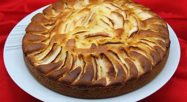 Un délicieux gâteau yaourt pomme, doré et appétissant, orné de fines lamelles de pommes disposées en rosace sur le dessus.